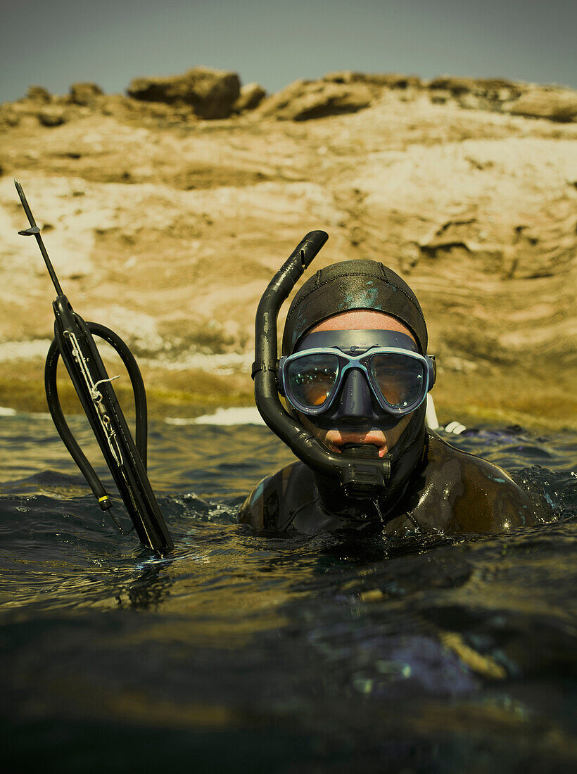 A spear fisher floats in the water with his spear gun.