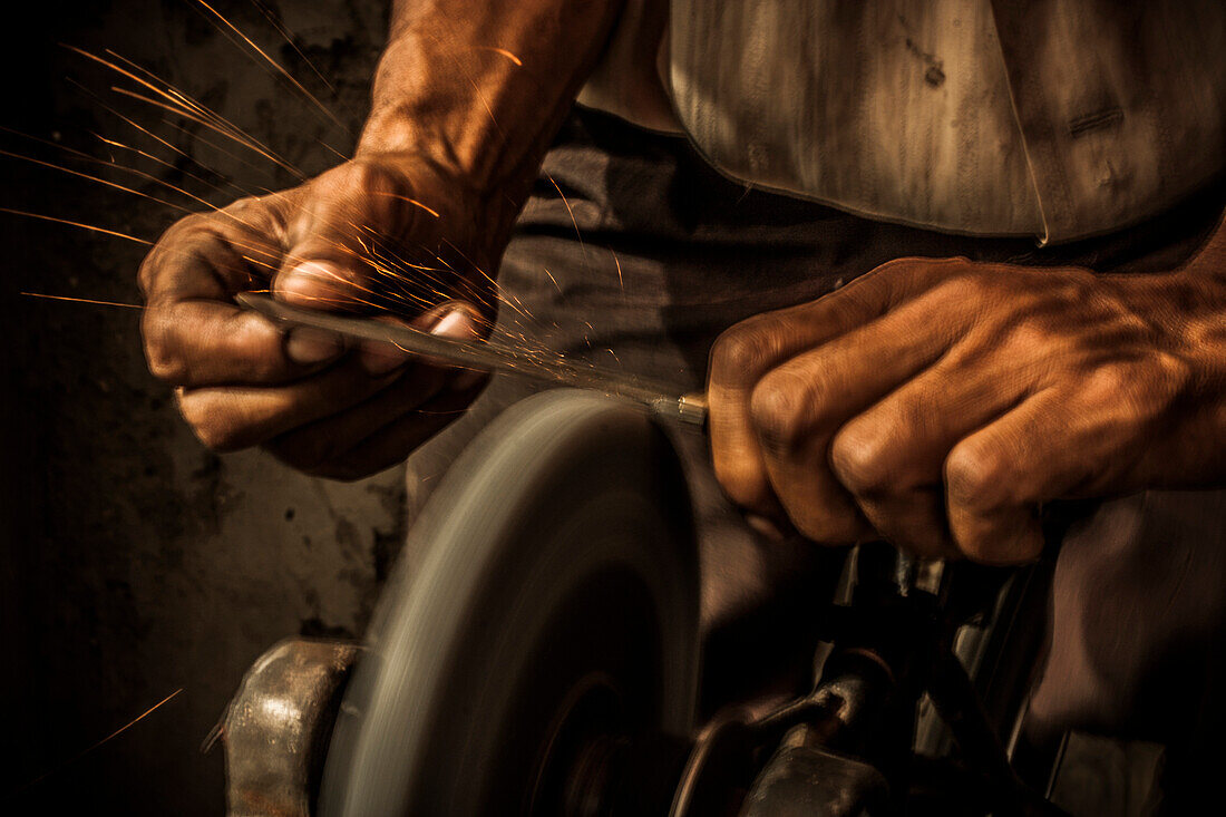 A man sharpening a knife on a grinding wheel powered by a bicycle drive chain.