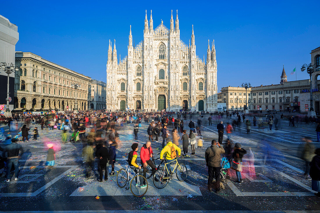 Cyclists in warm spring sun in front of the facade of the Gothic Duomo, Milan, Lombardy, Italy, Europe