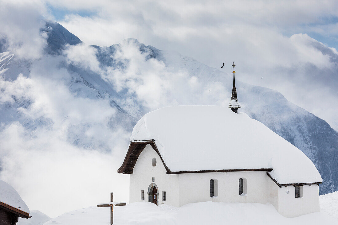 Clouds above the mountain huts and church covered with snow, Bettmeralp, district of Raron, canton of Valais, Switzerland, Europe