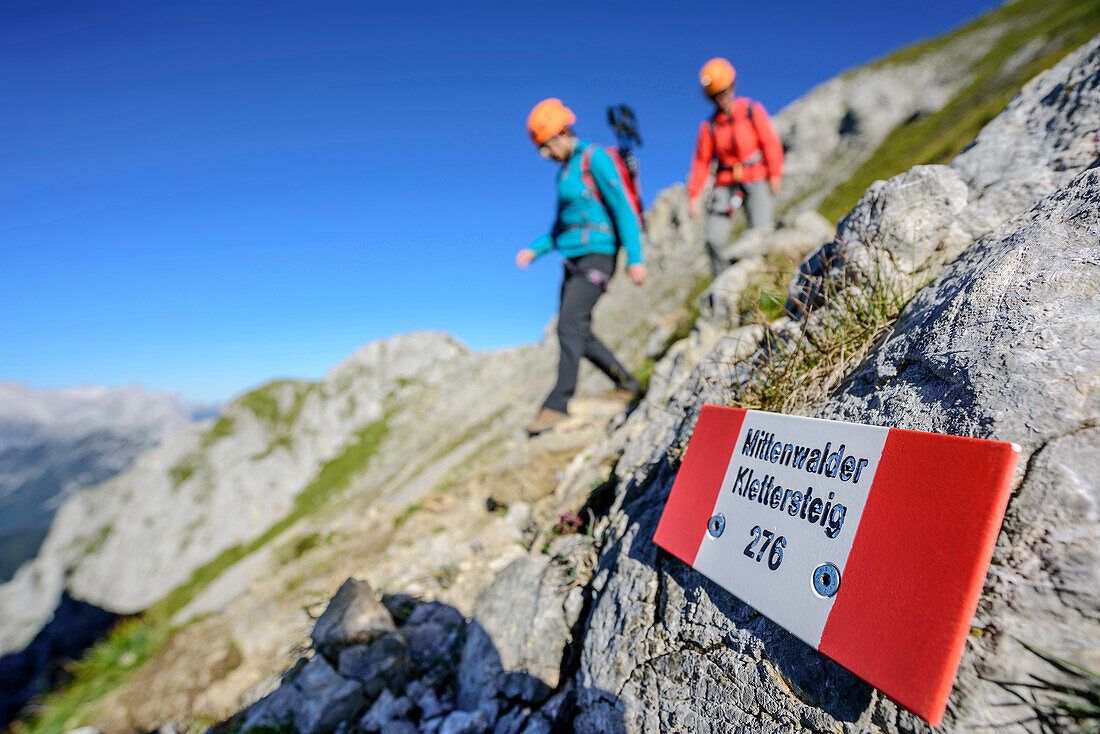 Signpost fixed-rope route Mittenwalder Klettersteig, two persons out of focus in background, fixed-rope route Mittenwalder Hoehenweg, Karwendel range, Upper Bavaria, Bavaria, Germany