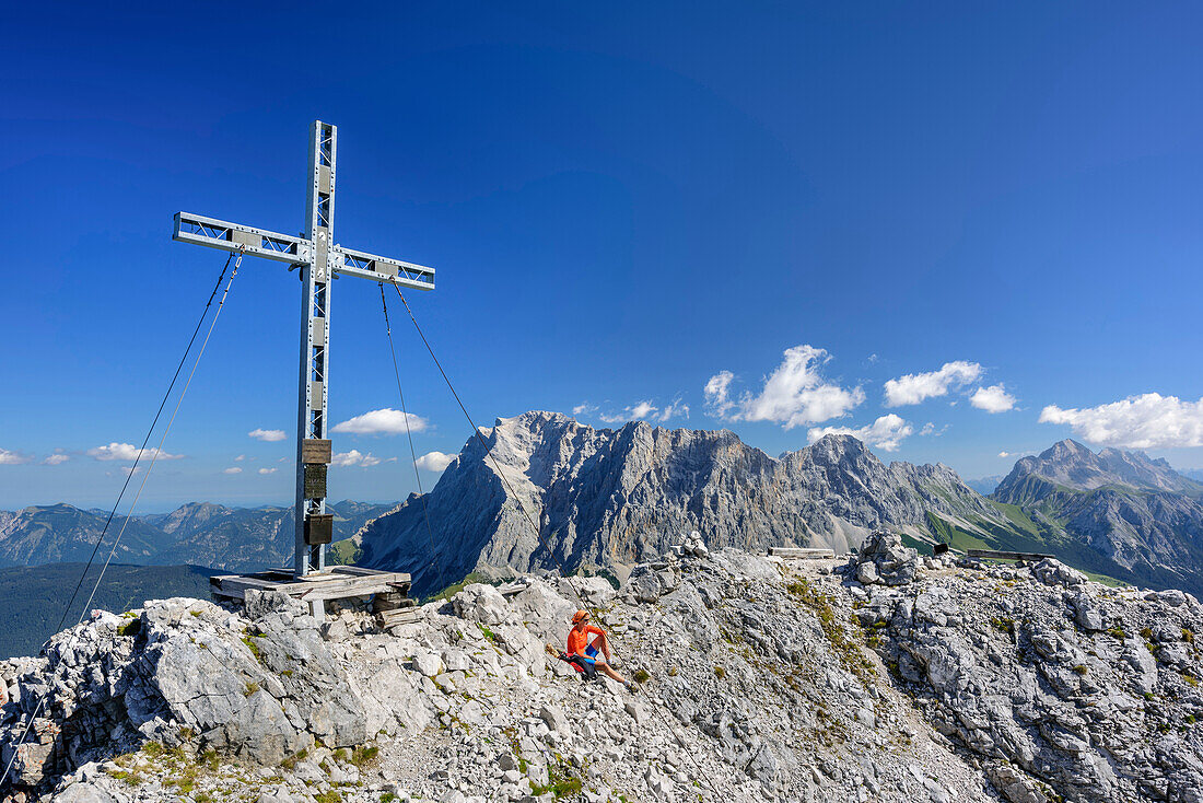 Frau sitzt am Gipfel der Ehrwalder Sonnenspitze, Wetterstein mit Zugspitze im Hintergrund, Ehrwalder Sonnenspitze, Mieminger Berge, Tirol, Österreich