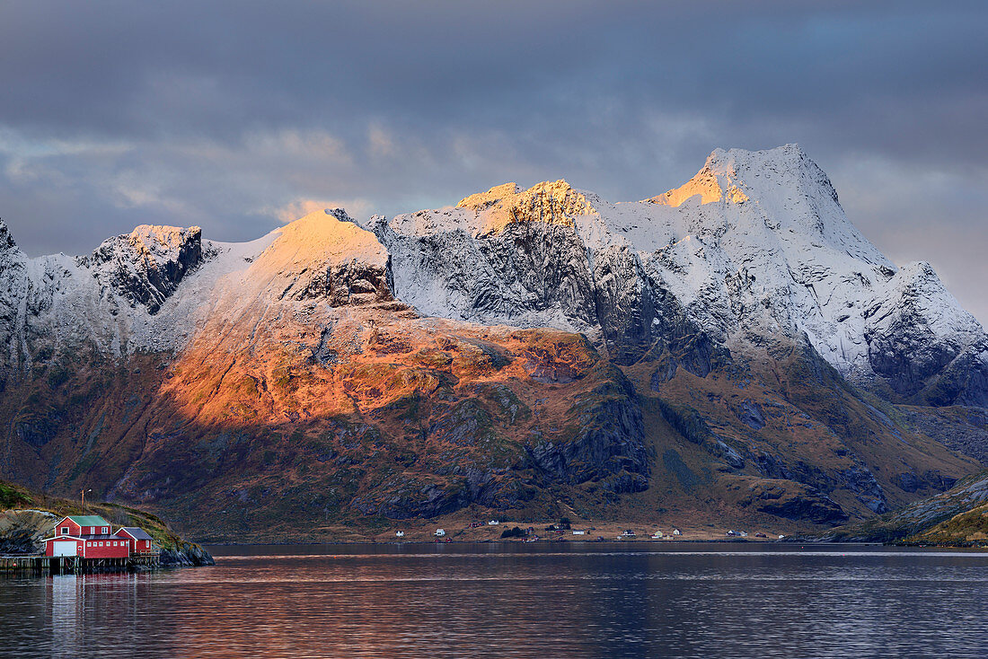 Meeresbucht mit Fischerhaus, verschneite Berge im Hintergrund, Hamnoy, Lofoten, Norland, Norwegen