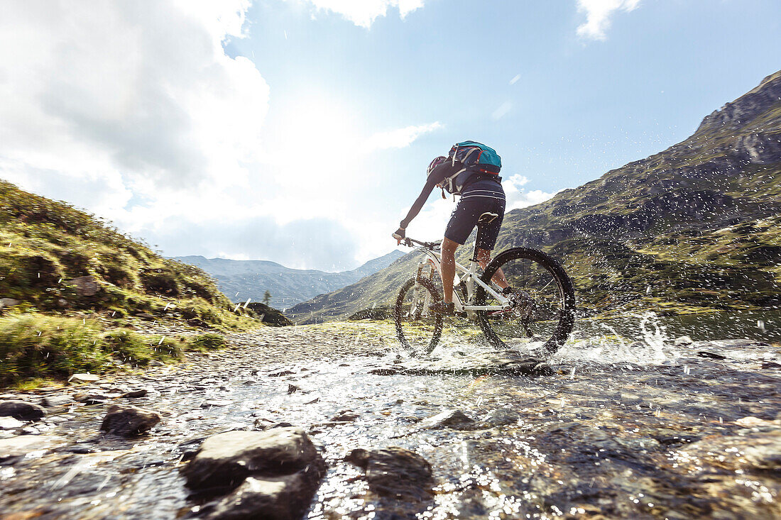 Mountainbikerin spritzt durch Gebirgsbach am Giglachsee, Niedere Tauern, Steiermark, Österreich