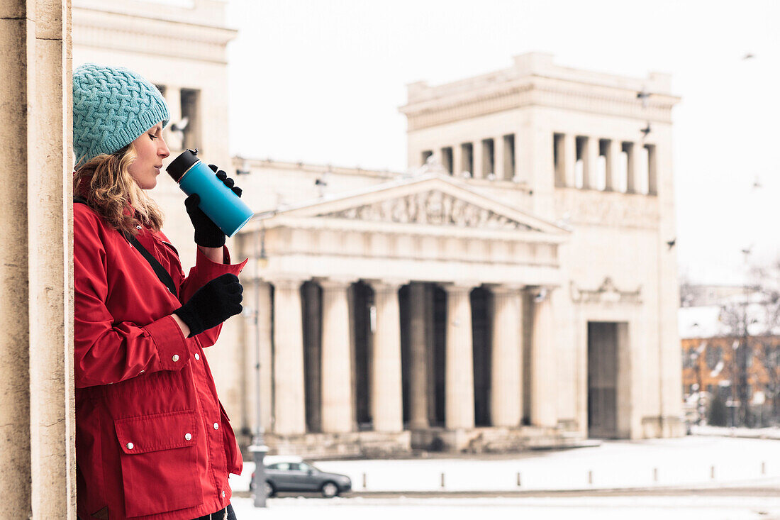 Young woman with coffee mug on snowy Königs Plaza in Munich, Bavaria, Germany