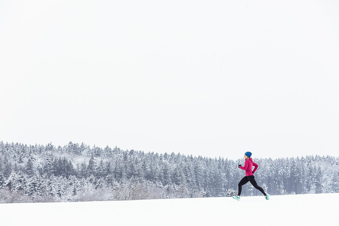 Junge Frau joggt durch verschneite Landschaft in Berg am Starnberger See, Bayern, Deutschland.