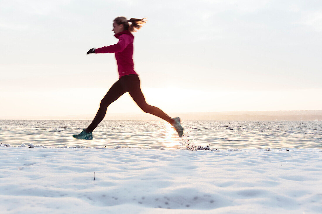 Junge Frau joggt am verschneiten Starnberger See, Bayern, Deutschland.