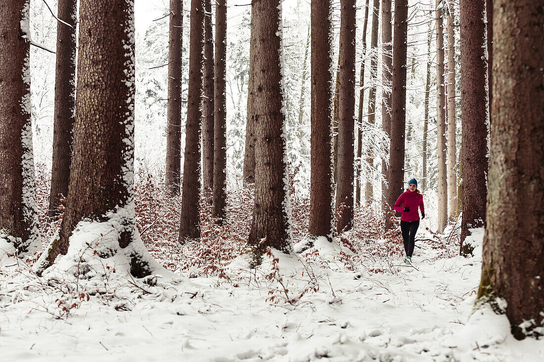 Junge Frau joggt durch verschneiten Wald in Berg am Starnberger See, Bayern, Deutschland.