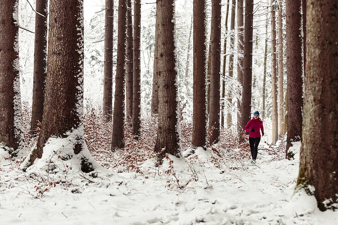 young woman running in snow-covered forest, Berg, Lake Starnberg, Bavaria, Germany.