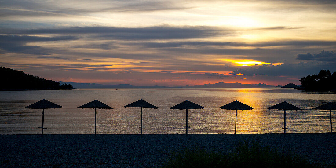 Silhouette of umbrellas on the beach at sunset on a greek island along the Aegean sea, Panormos, Thessalia Sterea Ellada, Greece