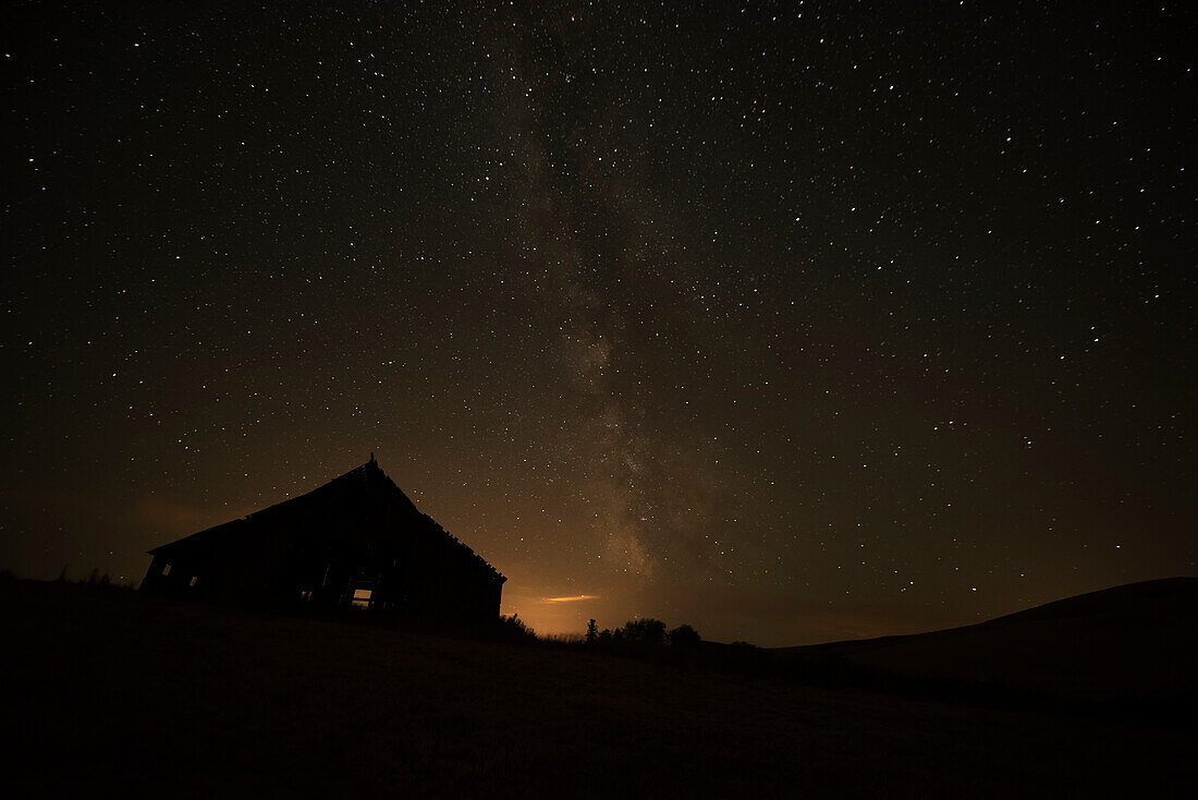 Night sky glowing over silhouette of a barn with a peaked roofline, Palouse, Washington, United States of America