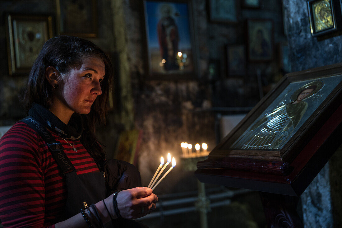 Young woman lighting candles in a small curch, Gudauri, Mtskheta-Mtianeti, Georgia