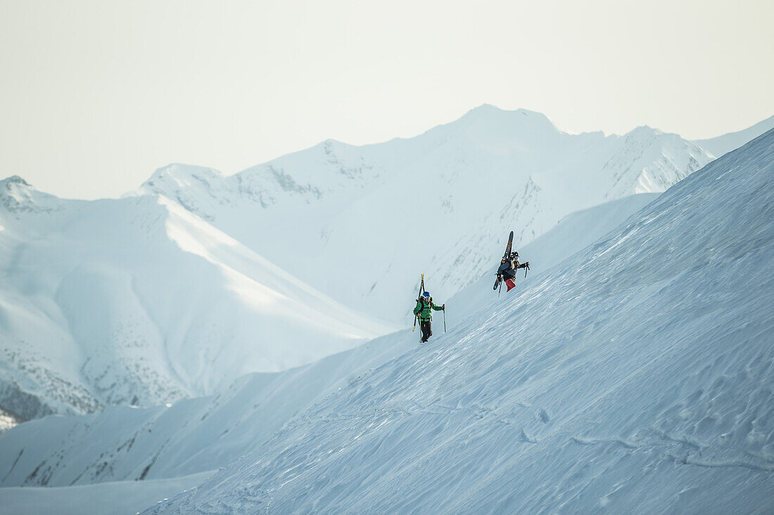 Zwei junge Skifahrer laufen durch den Tiefschnee auf den Gipfel eines Berges, Gudauri, Mzcheta-Mtianeti, Georgien