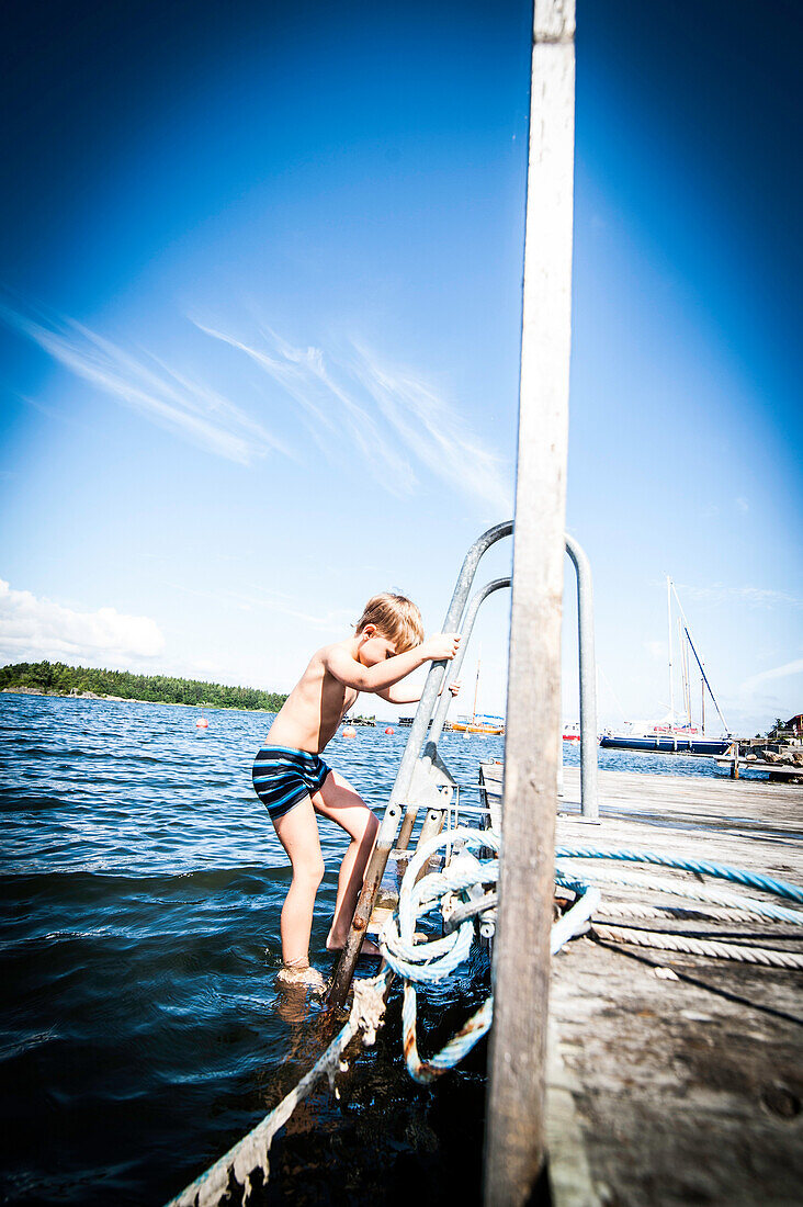Junge klettert vom Bootssteg in das Wasser, Öregrund, Uppsala, Schweden