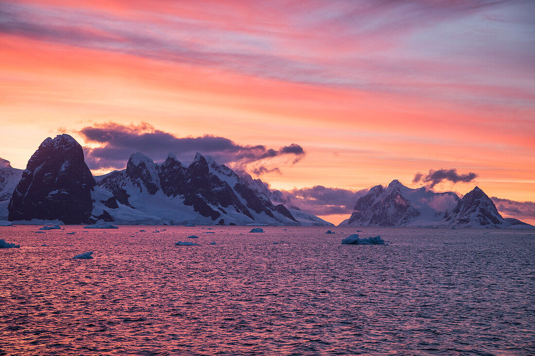 Eisberge und schneebedeckte Berge bei Sonnenuntergang, nahe Lemaire Kanal, Grahamland, Antarktische Halbinsel, Antarktis