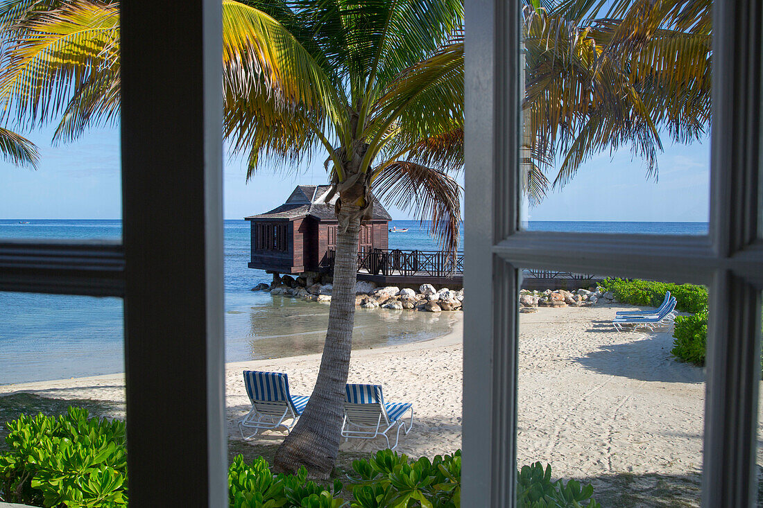 Palm trees and overwater spa cabana of Half Moon Resort seen through window of Royal Suite in Royal Court accomodation Rose Hall, near Montego Bay, Saint James, Jamaica