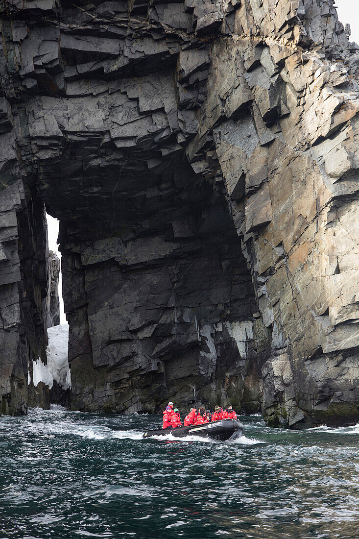 Zodiac raft excursion for passengers of expedition cruise ship MV Sea Spirit (Poseidon Expeditions) along rock wall with opening Spert Island, near Trinity Island, Palmer Archipelago, South Shetland Islands, Antarctica