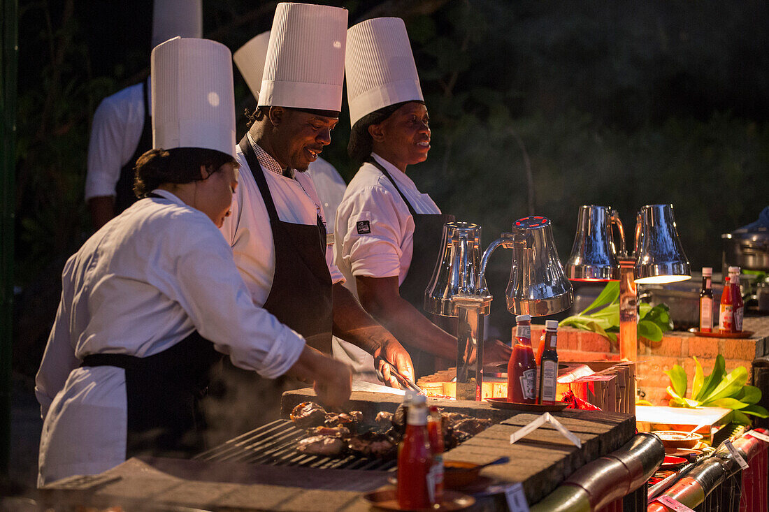 Köchinnen und Köche grillen Fleisch beim Beach Barbecue Abendessen am Strand vom Half Moon Resort, Rose Hall, nahe Montego Bay, Saint James, Jamaika