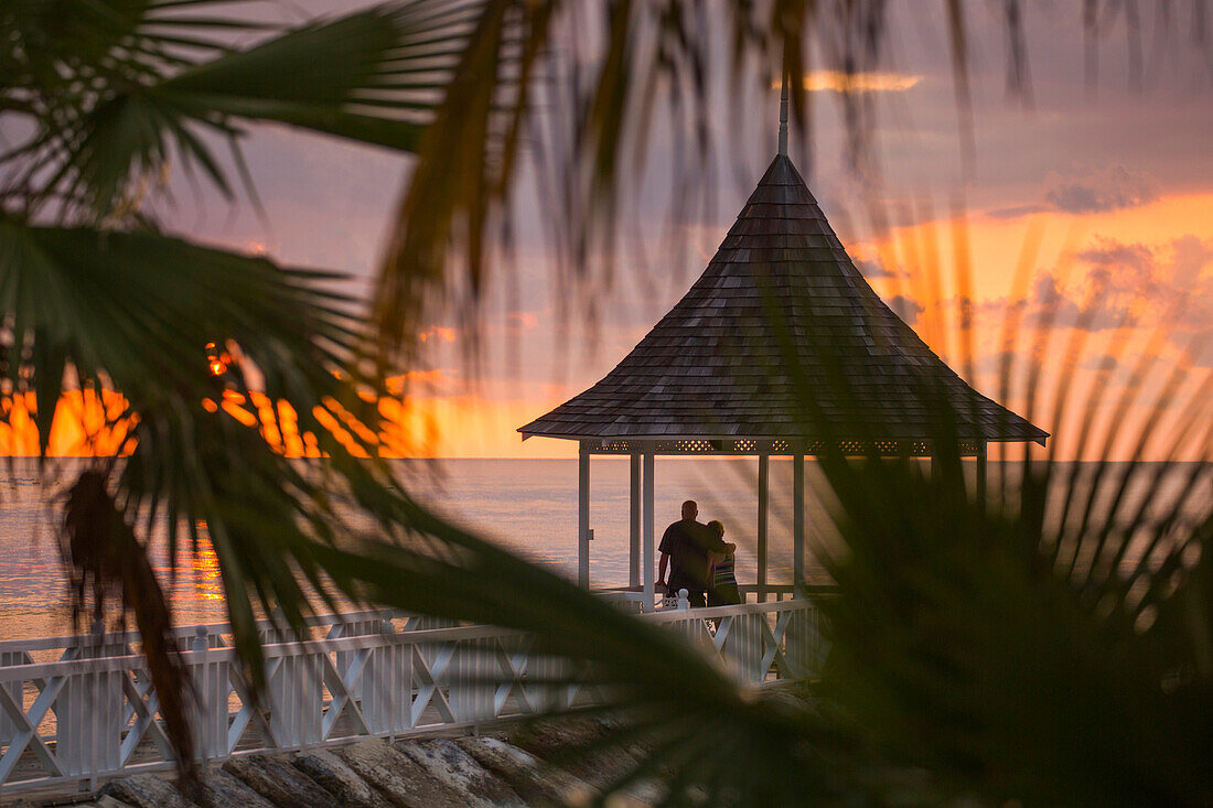Couple admire sunset from pavillion on jetty at Half Moon Resort Rose Hall, near Montego Bay, Saint James, Jamaica