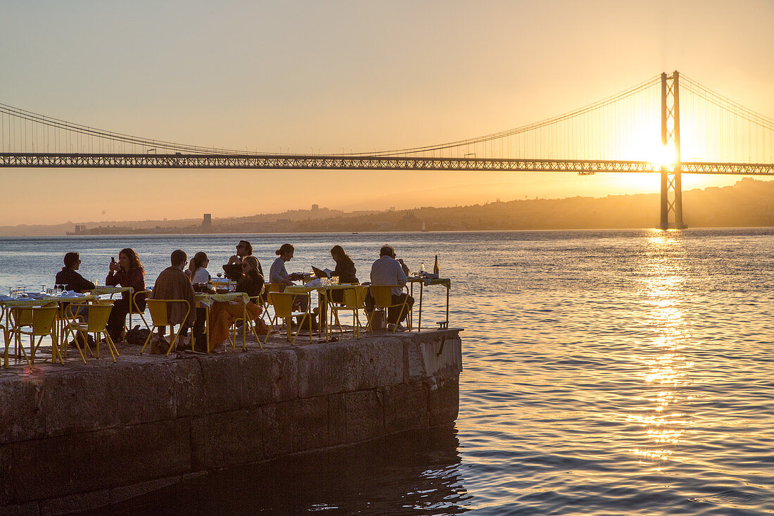 sunset on riverfront restaurant Ponto Final, view from south bank of River Tagus,and the 25th April Bridge, Cacilhas, Almada, Lisbon, Portugal