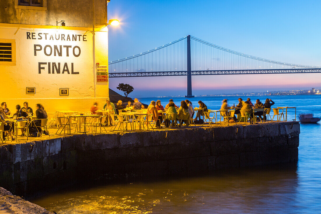 sunset on riverfront restaurant Ponto Final, view from south bank of River Tagus, and the 25th April Bridge, Cacilhas, Almada, Lisbon, Portugal