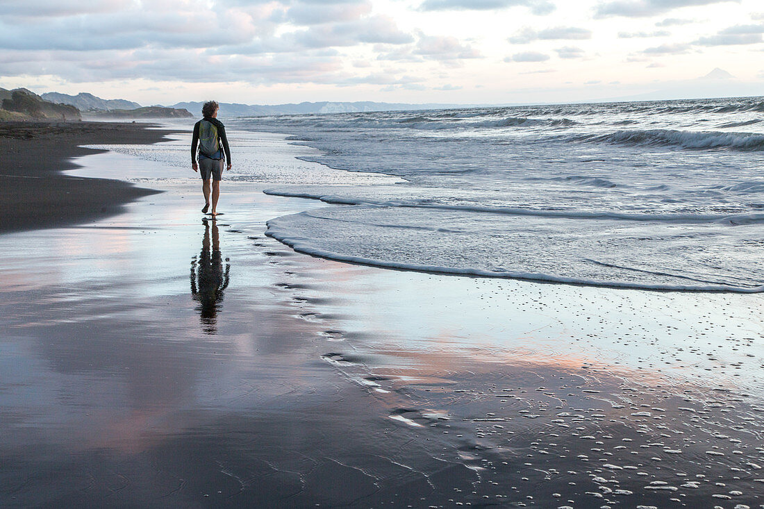 einsamer Wanderer, Frau, Mensch, Abendrot, Ebbe am Strand, schwarzer Sand, Fußspuren, Sonnenuntergang, Dämmerung, Silhouette, Westküste der Nordinsel, Neuseeland