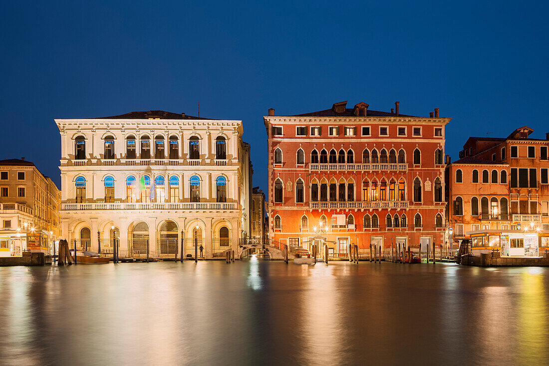 Blick über den Canal Grande mit den beleuchteten Fassaden des Palazzo Dolfin Manin und des Palazzo Bembo (von links) im Blau der Dämmerung, San Marco, Venedig, Venezien, Italien