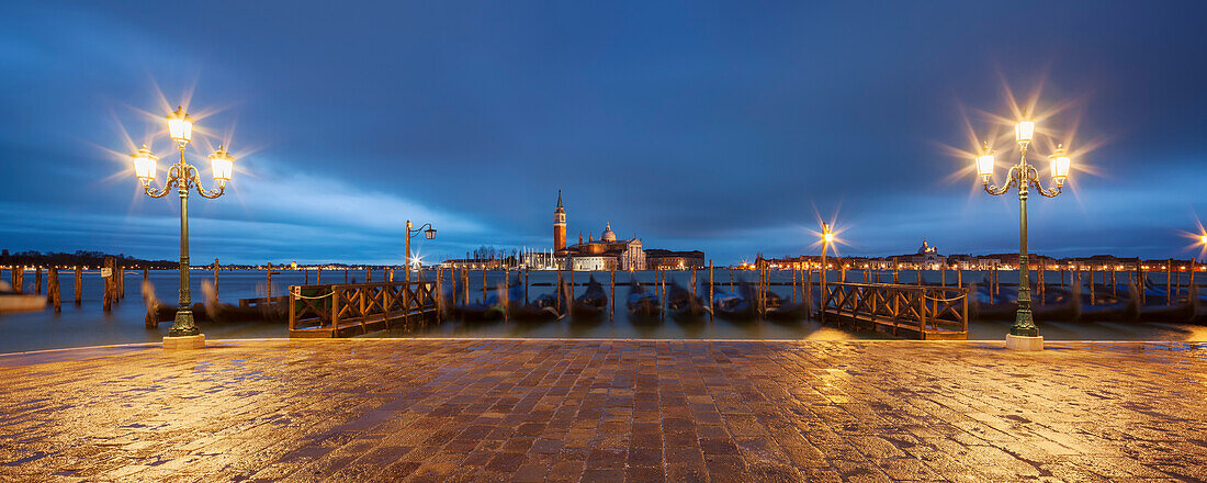 Panoramic view from St. Mark's Square with gondolas and lanterns to the island of San Giorgio Maggiore with its namesake church in the blue of the night, San Marco, Venice, Veneto, Italy