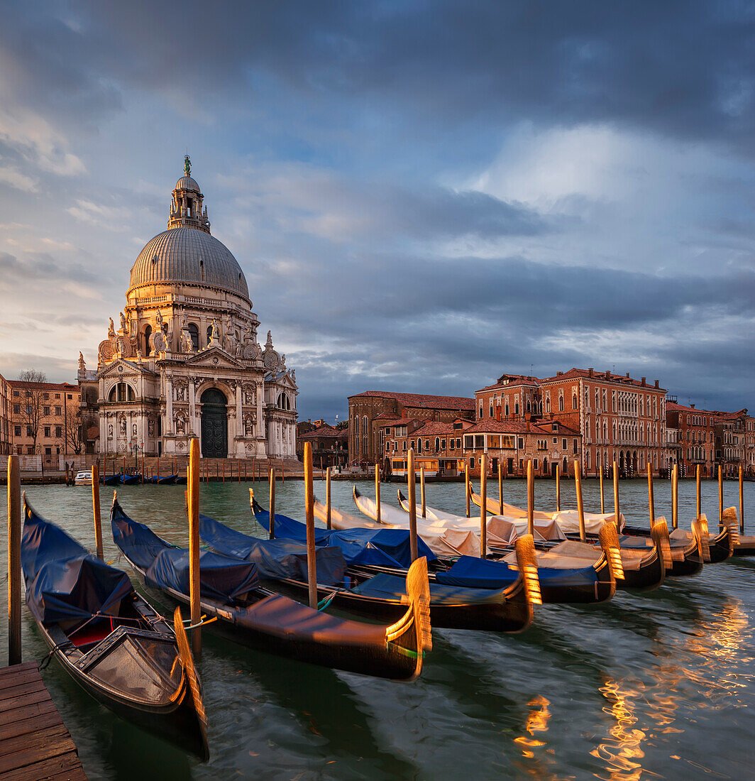 View over the Grand Canal to the Church of Santa Maria della Salute with gondolas in the morning sun and dramatic clouds, San Marco, Venice, Veneto, Italy
