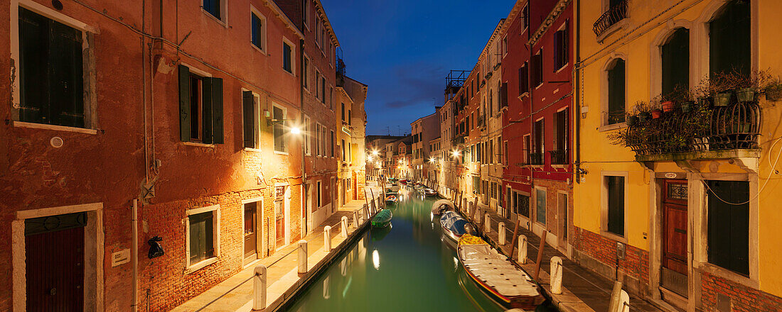 Panorama of illuminated house facades and boats on the canal Rio Ognissanti in blue twilight, Dorsoduro, Venice, Veneto, Italy