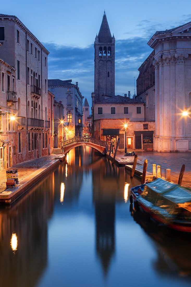 Illuminated houses of the Rio di San Barnaba with the tower of the church of Santa Maria dei Carmini and boats in the blue dusk, Dorsoduro, Venice, Veneto, Italy