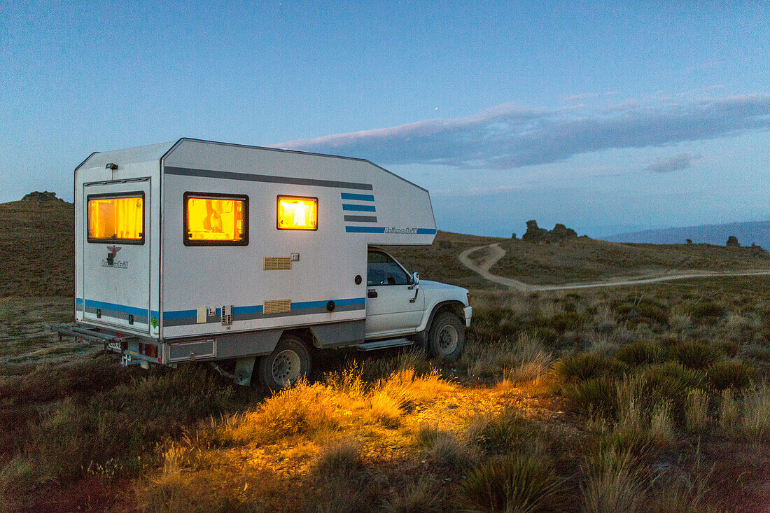Allrad-Camper, wildes Camping, nachts, beleuchtete Fenster, Wohnmobil an der Nevis Road, Passhöhe, Abendsonne, Tussockgras Landschaft, Central Otago, Südinsel, Neuseeland