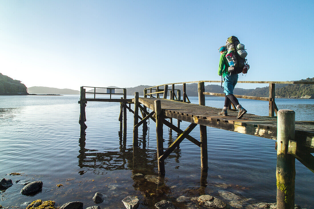 tramper with backpack, water taxi pick up point, jetty, wilderness, Stewart Island, Rakiura, New Zealand