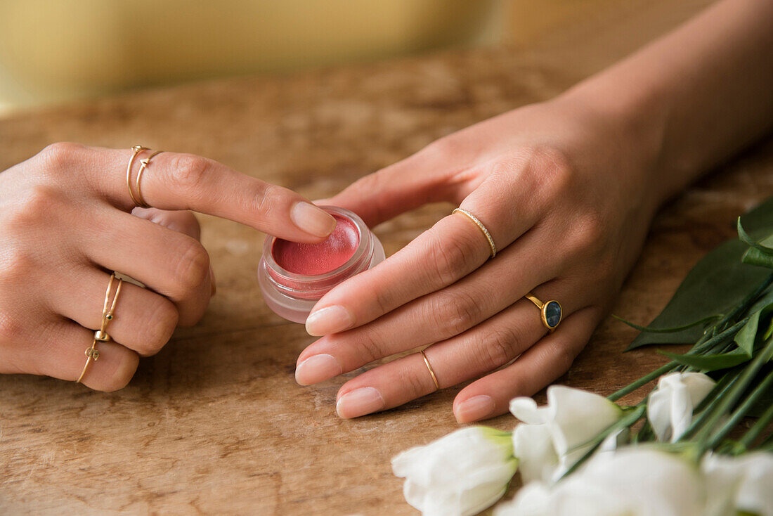 Hands of Hispanic woman holding jar of lip gloss