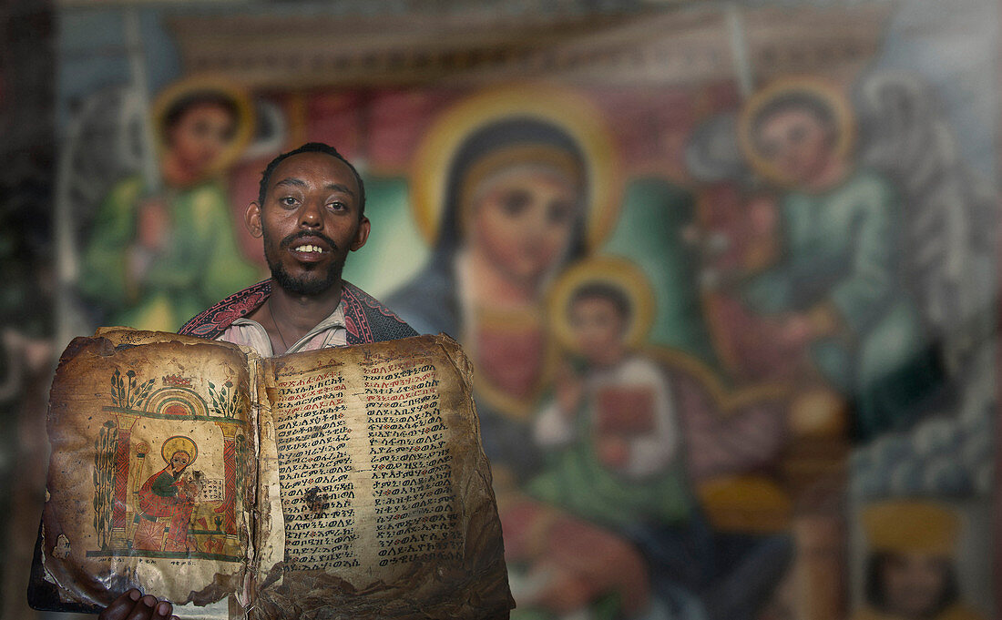 Black man holding worn religious book near mural