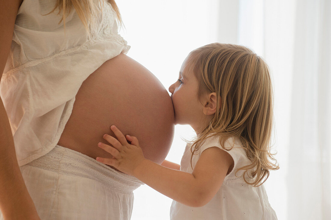 Caucasian girl kissing belly of pregnant mother