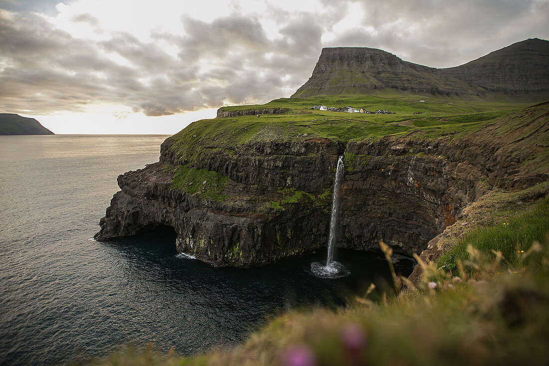 Wasserfall fließt von einer hohen Klippe ins Meer, Färöer Inseln