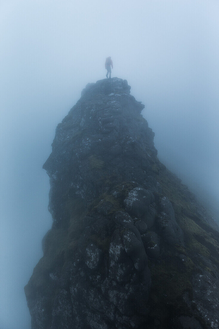 Person steht auf der Spitze eines Felsens an einem nebligen Tag, Färöer Inseln