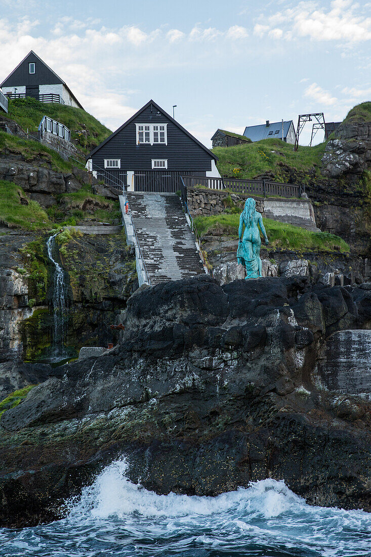 Statue of a woman on a rock in the sea in front of a village, Faeroe Islands