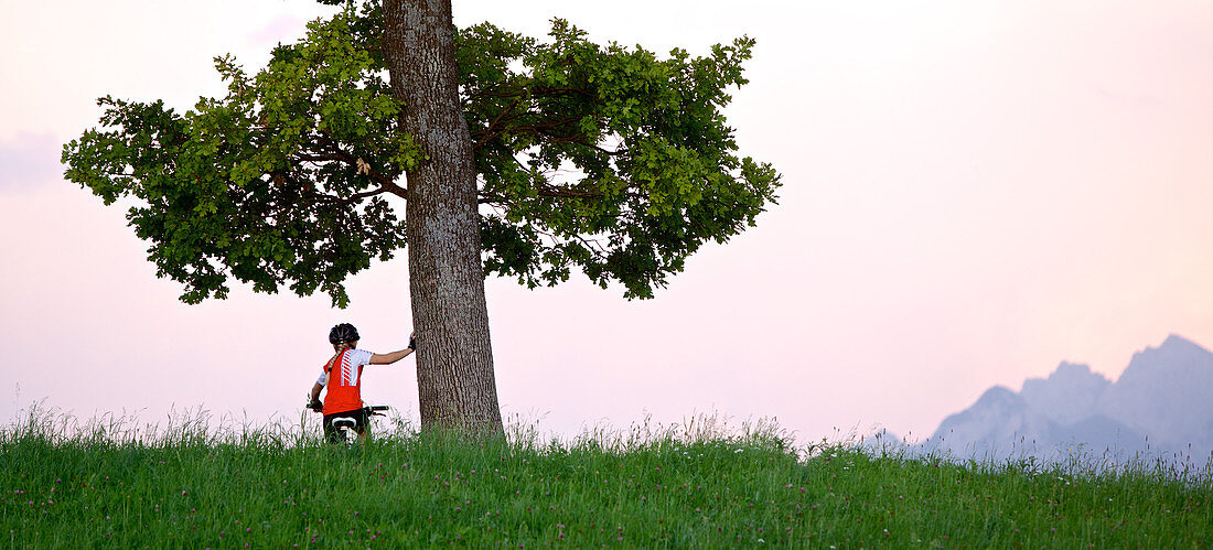 Mädchen sitzt auf ihrem Fahrrad und hält sich an einem Baum fest, Füssen, Bayern, Deutschland