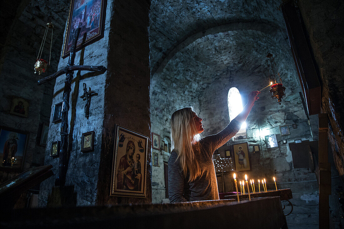 Young woman lighting a candle in a small church, Gudauri, Mtskheta-Mtianeti, Georgia