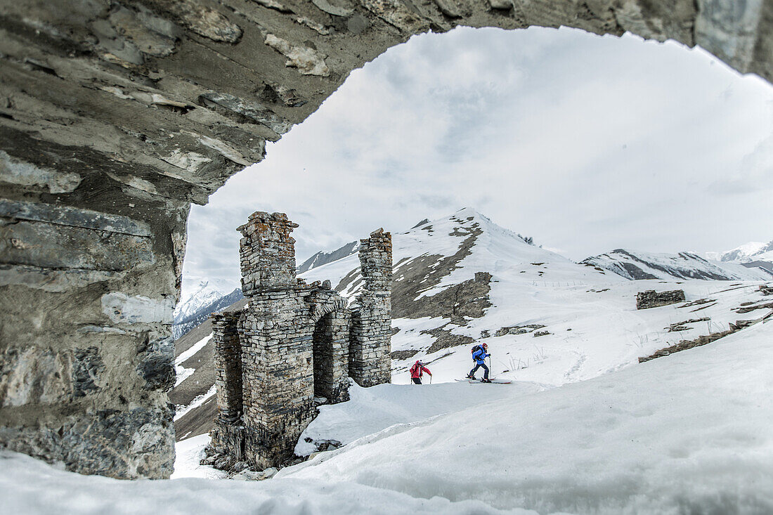 Zwei junge Skifahrer laufen an einer Ruine in den Bergen vorbei, Gudauri, Mzcheta-Mtianeti, Georgien