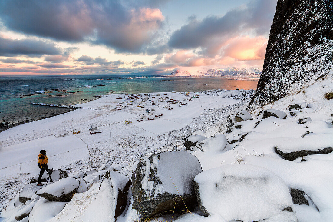 Fotograf auf dem Schnee bewundert das Fischerdorf unter einem bunten Himmel Eggum, Vestvagoy (Vest-Vagoy) Insel, Lofoten Inseln, Arktis, Norwegen, Skandinavien, Europa