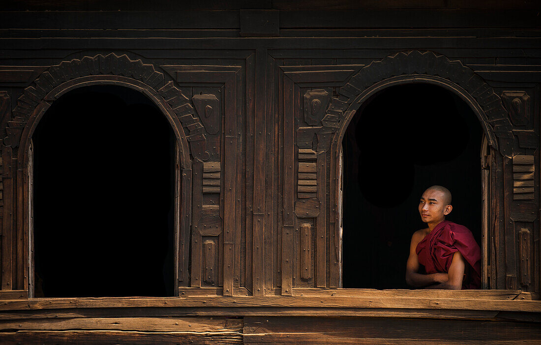 Ein Mönch schaut aus dem Fenster eines hölzernen Klosters in der Nähe von Bagan (Pagan), Myanmar (Burma), Asien