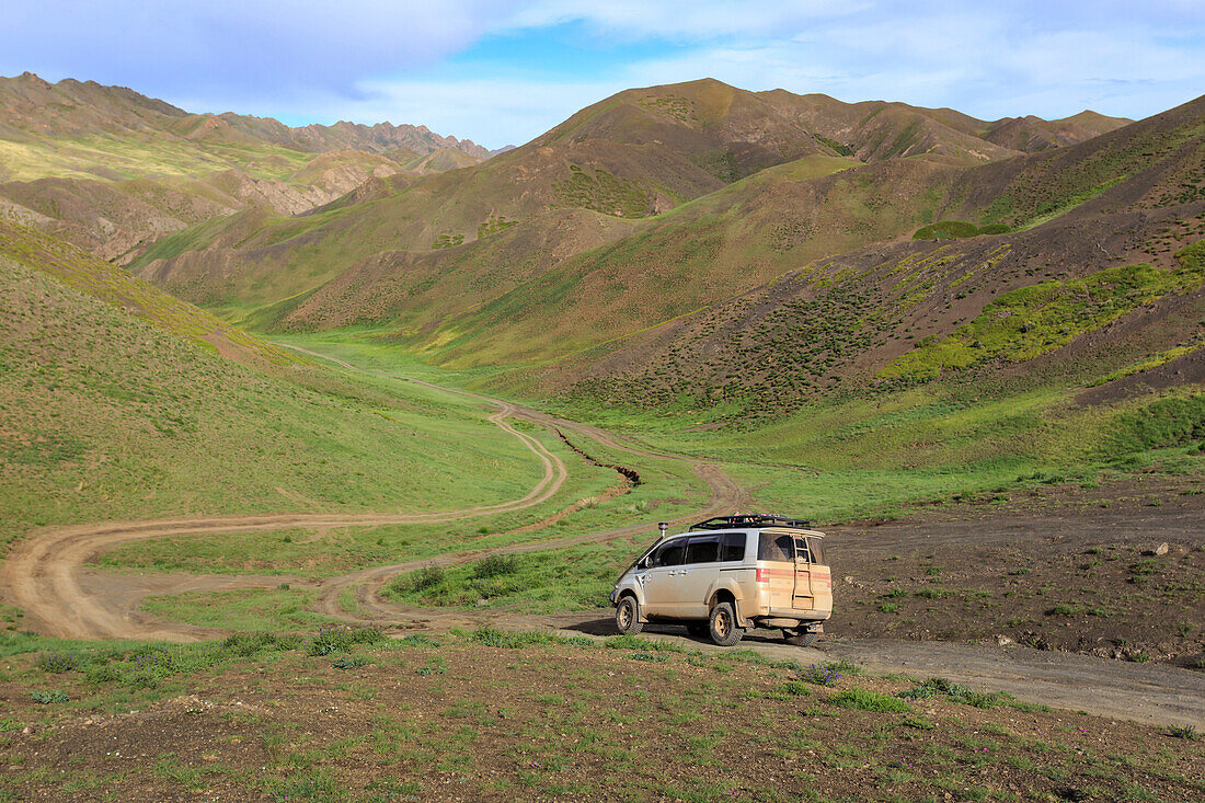 Fahrzeug fährt auf der Straße durch üppige Berge, Gurvan Saikhan Nationalpark, in der Nähe von Yolyn Am (Yol Valley), Gobi-Wüste, Mongolei, Zentralasien, Asien