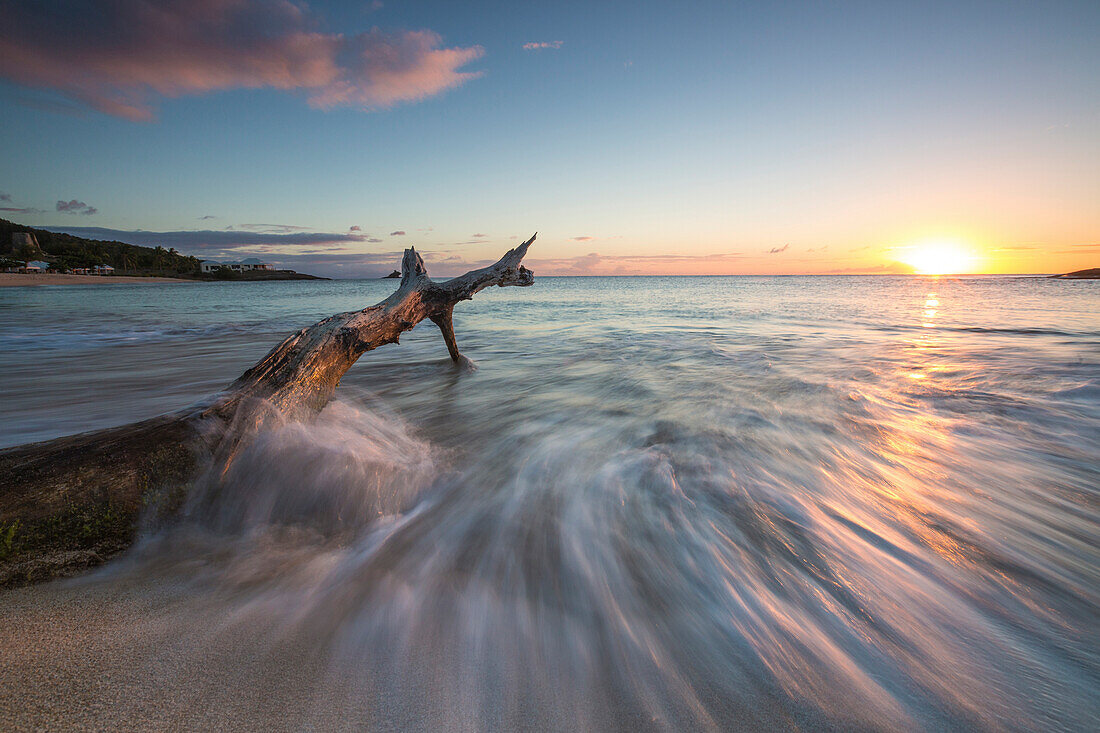 Wellen auf einem Baumstamm am Strand umrahmt von der Karibik Sonnenuntergang, Hawksbill Bay, Antigua, Antigua und Barbuda, Leeward Inseln, Westindische Inseln, Karibik, Mittelamerika