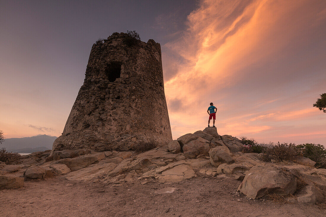 Wanderer bewundert Sonnenuntergang vom Steinturm mit Blick auf die Bucht, Porto Giunco, Villasimius, Cagliari, Sardinien, Italien, Mittelmeer, Europa