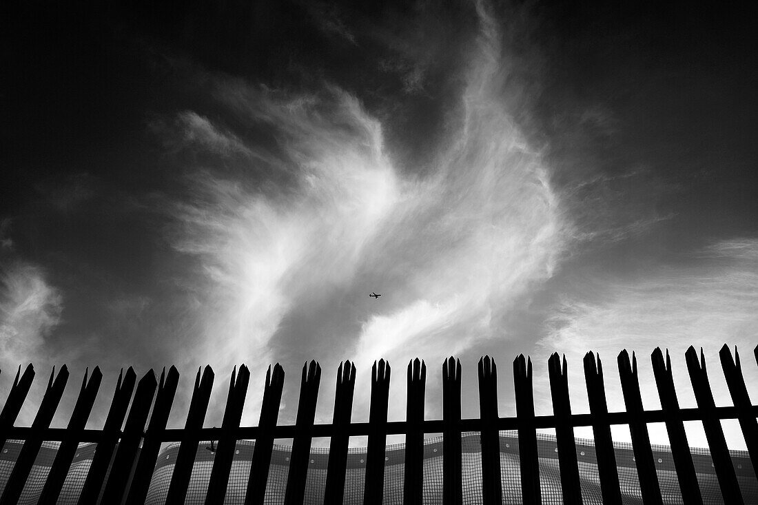 Industrial area with fence. Airplane flying in a cloudy sky. London, England