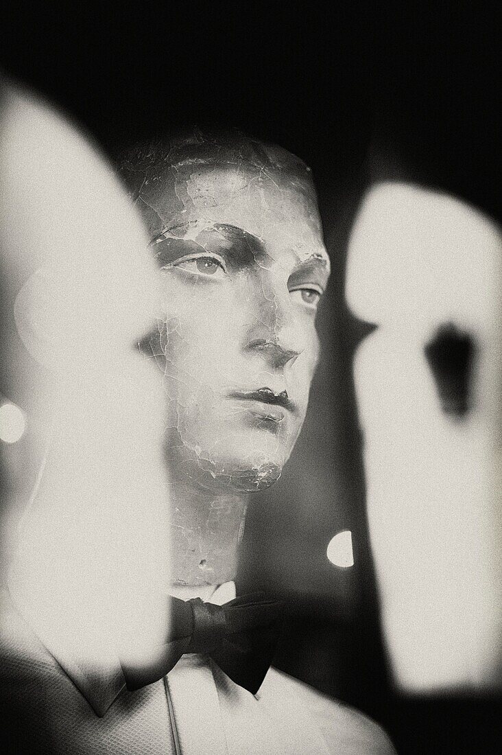 Old mannequin in shop window with hat and bow tie, reflections on glass