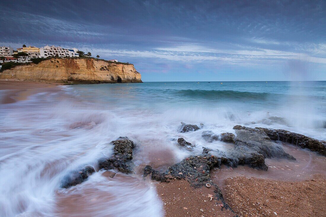 Ocean waves crashing on rocks and beach surrounding Carvoeiro village at sunset Lagoa Municipality Algarve Portugal Europe.